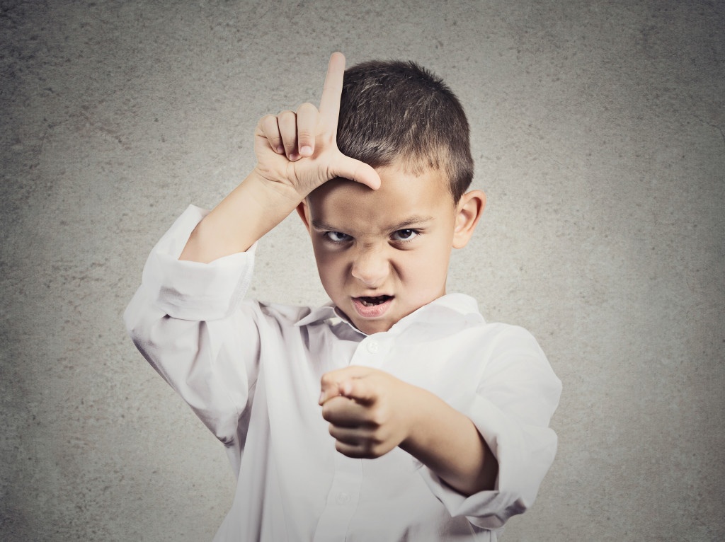Closeup portrait angry young Unhappy boy, young student displaying Loser Sign on forehead, pointing at you with disgust isolated grey wall background. Negative human emotion, expression Body Language